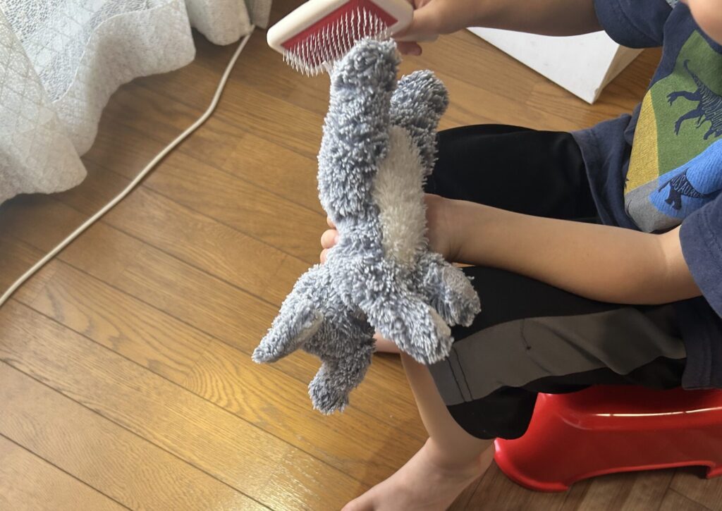 子どもがAURORAのぬいぐるみにスリッカーブラシで毛並みを整えている様子